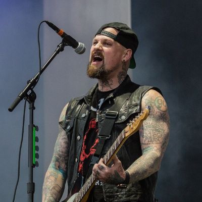 Benji Madden singing an playing guitar during an event. Image Source: Wikipedia